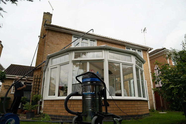 SkyVac vacuum pole clearing a house gutter from the ground, with the SkyVac machine in the foreground